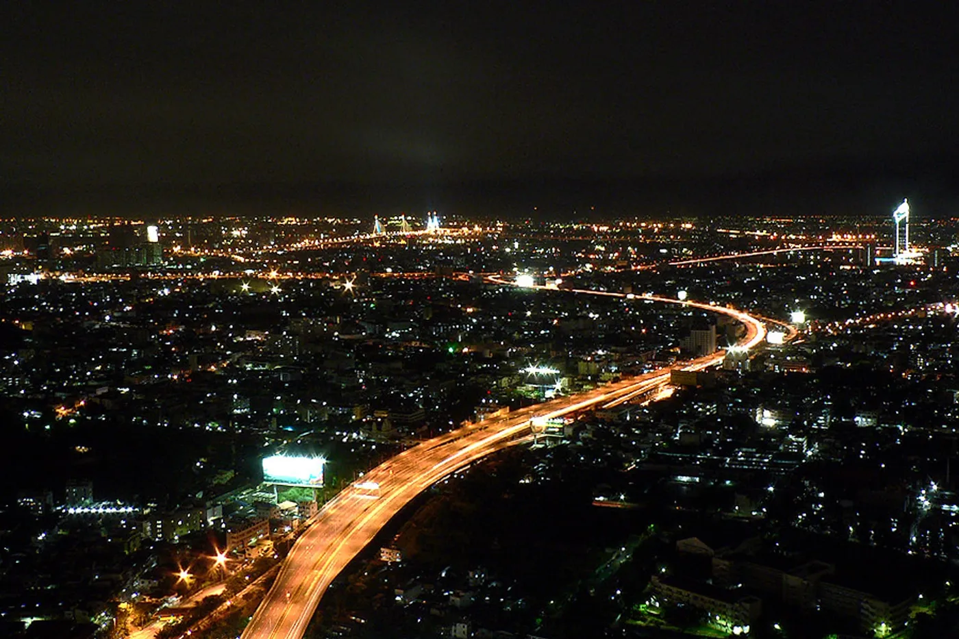 Bangkok from the roof at night, lights on, a hand rail in the foreground.
