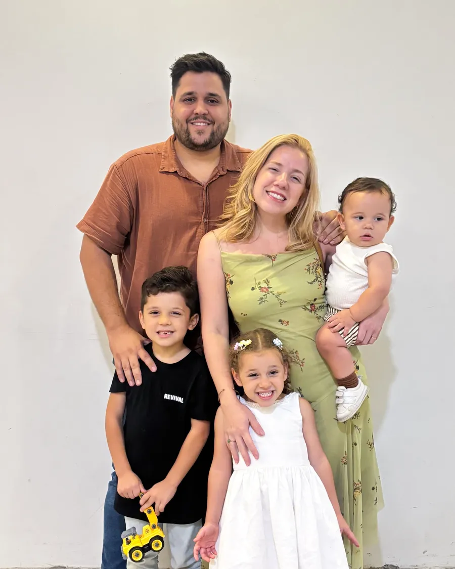 Lucas and Sara Baptista with their three children, smiling, against a plain white wall.